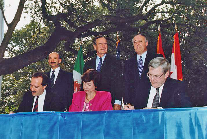 NAFTA Initialing Ceremony, October 1992. From left to right (standing) Mexican President Carlos Salinas de Gortari, US President George H. W. Bush, Canadian Prime Minister Brian Mulroney. (Seated) Jaime Serra Puche, Carla Hills, Michael Wilson. Photo courtesy of UNCTAD